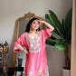 Woman in a pink traditional outfit standing in a room with a mirror and plant.